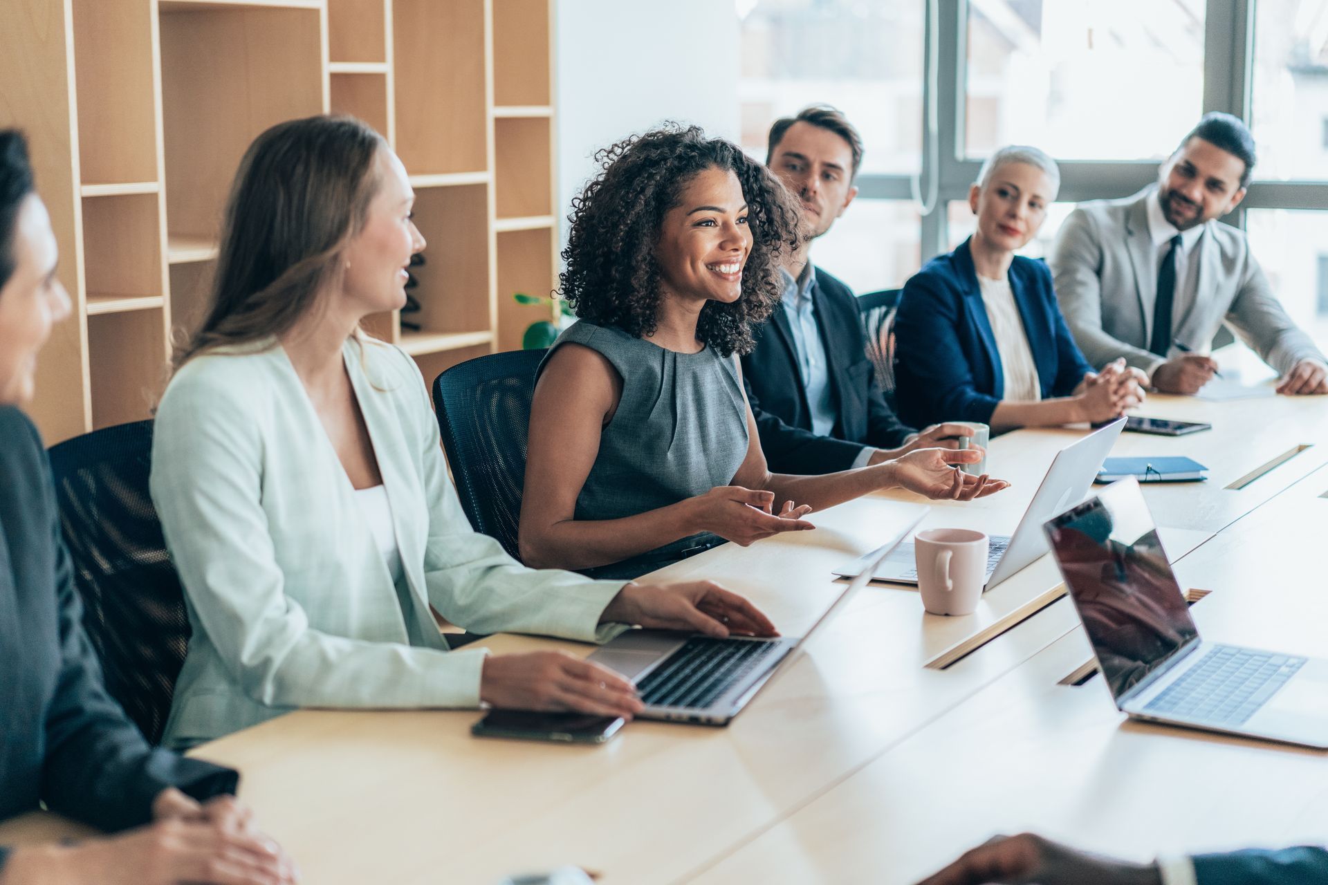 A diverse group of employees sit at a table, engaging in a business meeting using IST Confirm