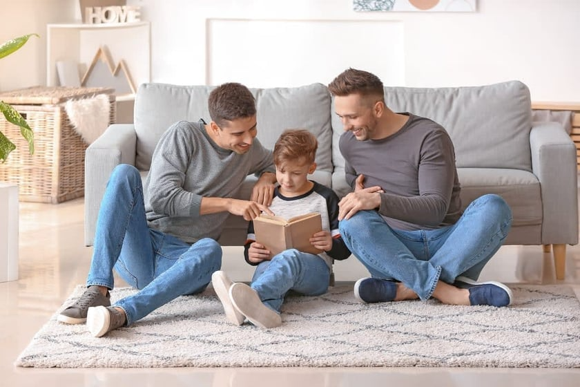 Three men are sitting on the floor reading a book to a little boy.