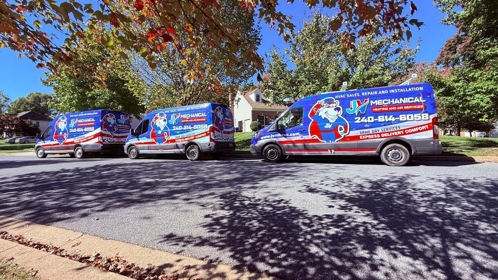 Three branded service vans parked in a row on a sunny residential street lined with trees.
