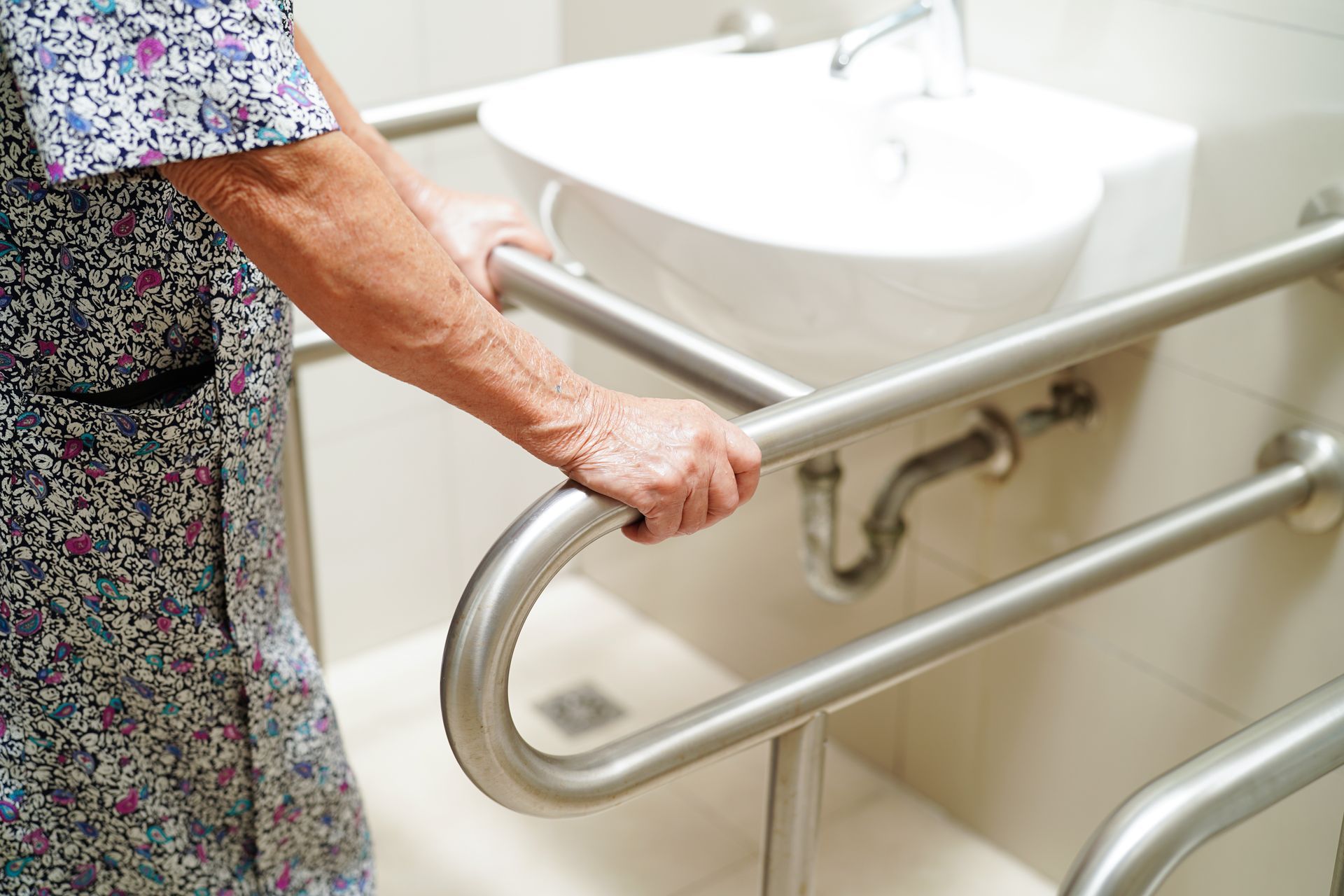Elderly person gripping bathroom grab bars near sink.