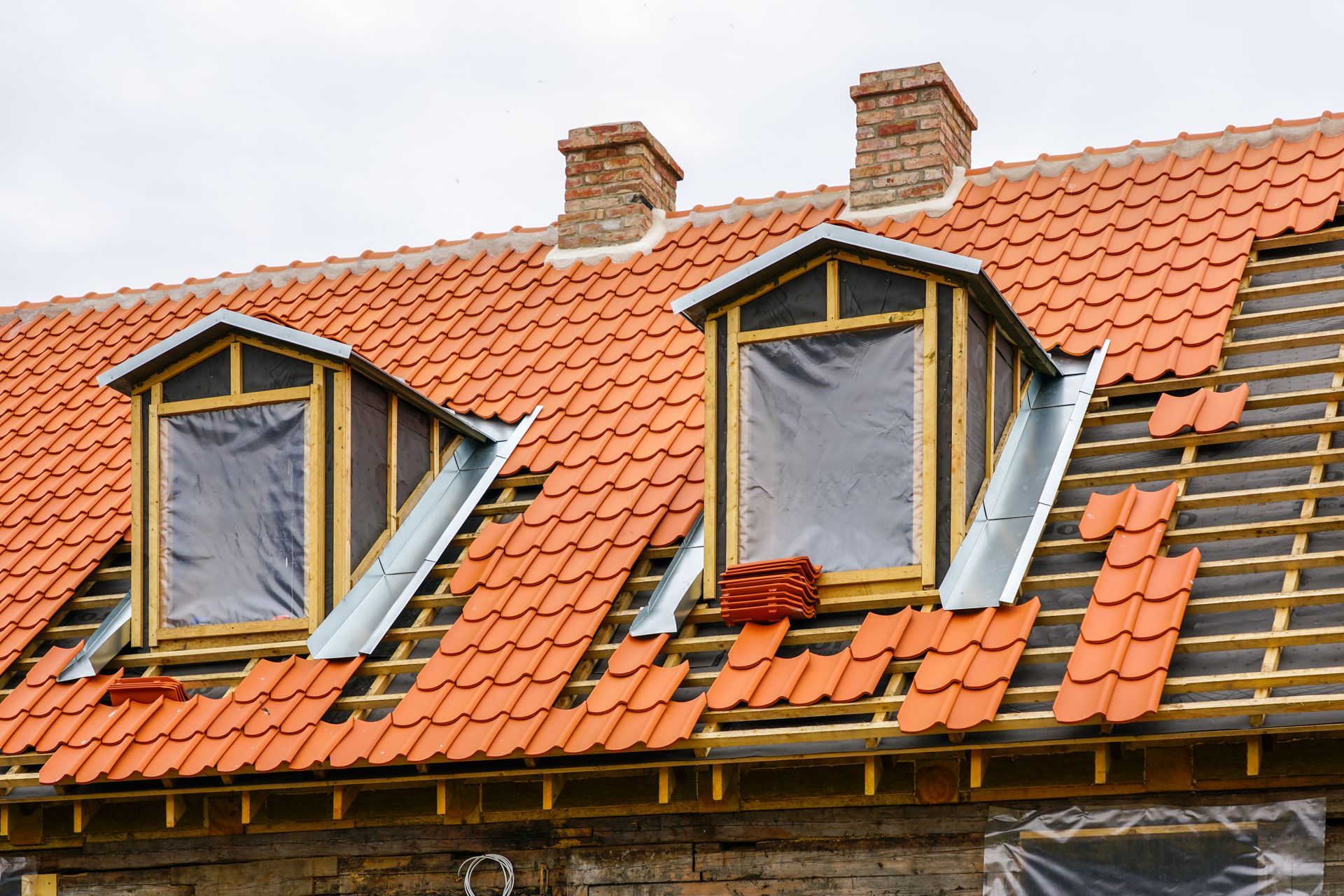 Roof being renovated with two dormers and red tiles.