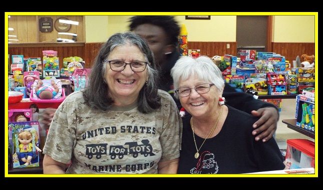 Two women are posing for a picture in front of a table full of toys.