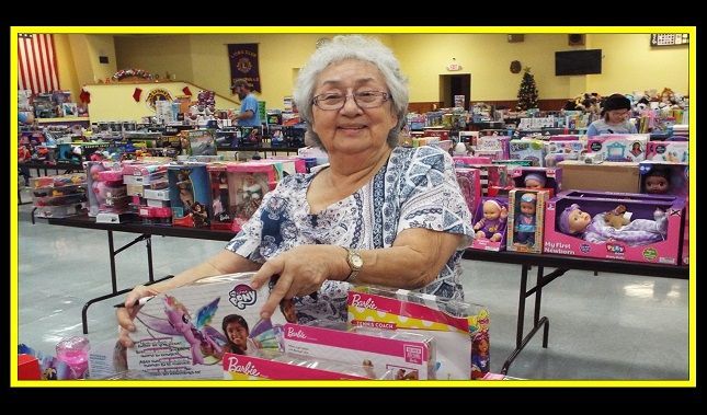 An elderly woman is standing in front of a table full of toys.