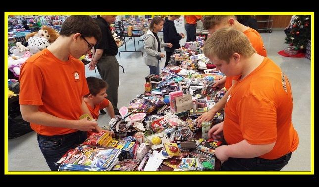 A group of people in orange shirts are looking at a table full of toys.