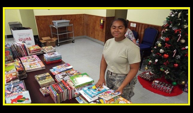 A woman in a military uniform is standing in front of a table full of books and a christmas tree