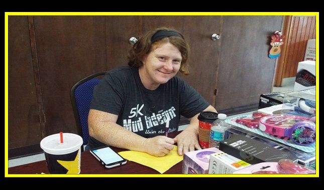 A woman is sitting at a table with a cup of soda and a cell phone.