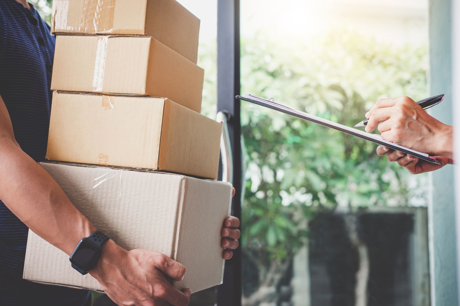 A delivery man is holding a stack of boxes and a clipboard.