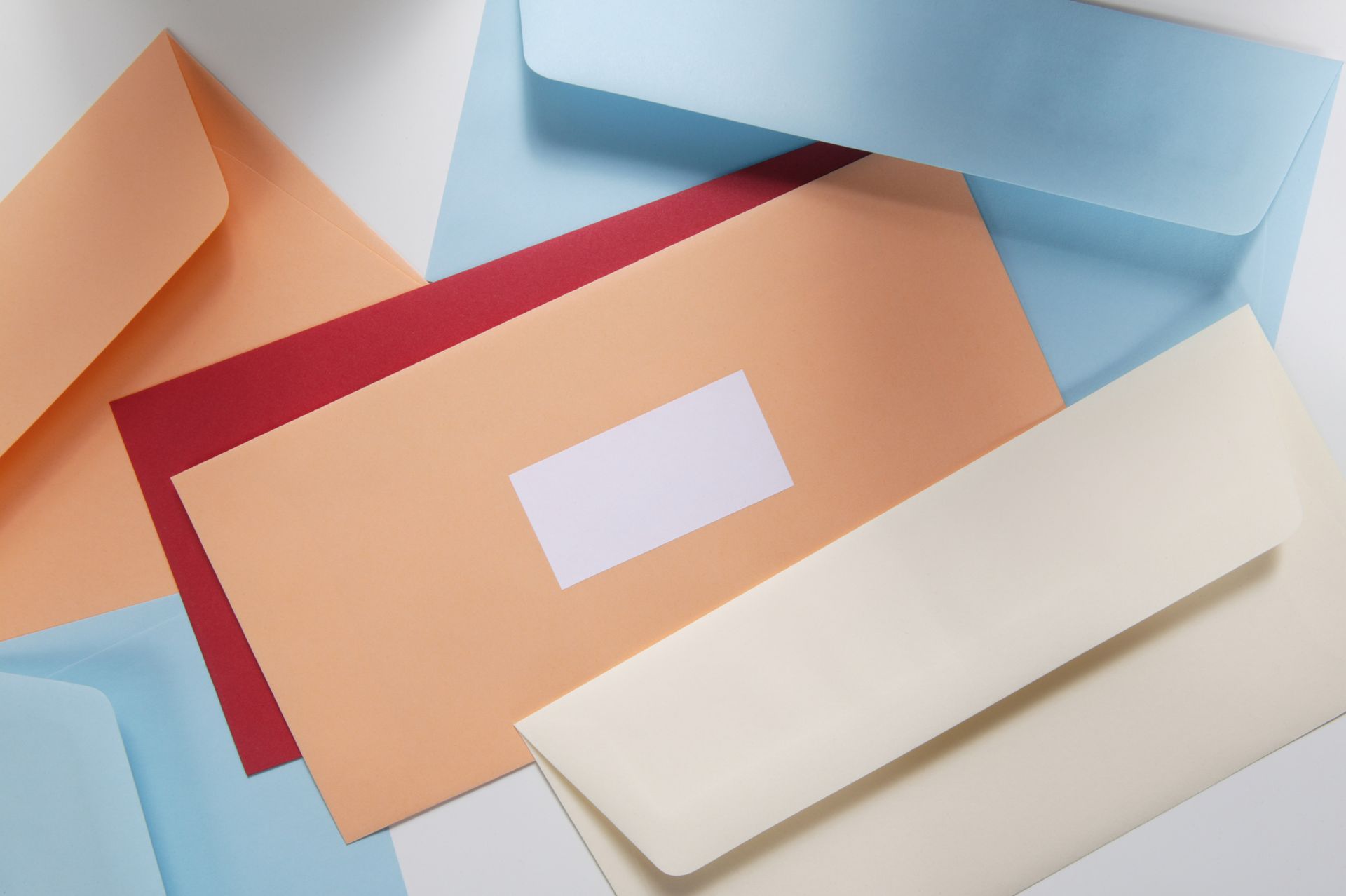 Assorted colorful envelopes, including peach, red, and blue, scattered on a white surface.