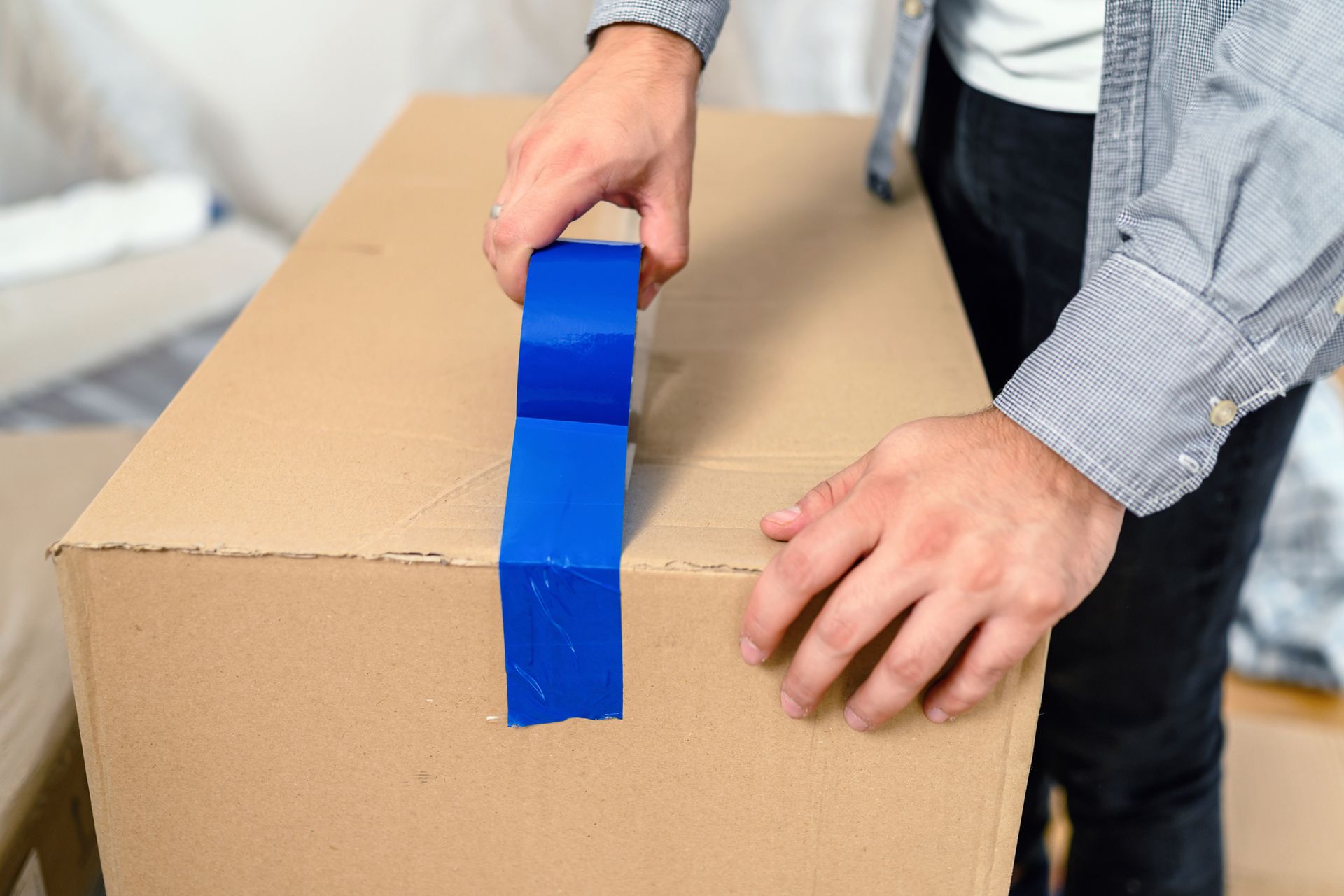 A man is taping a cardboard box with blue tape.
