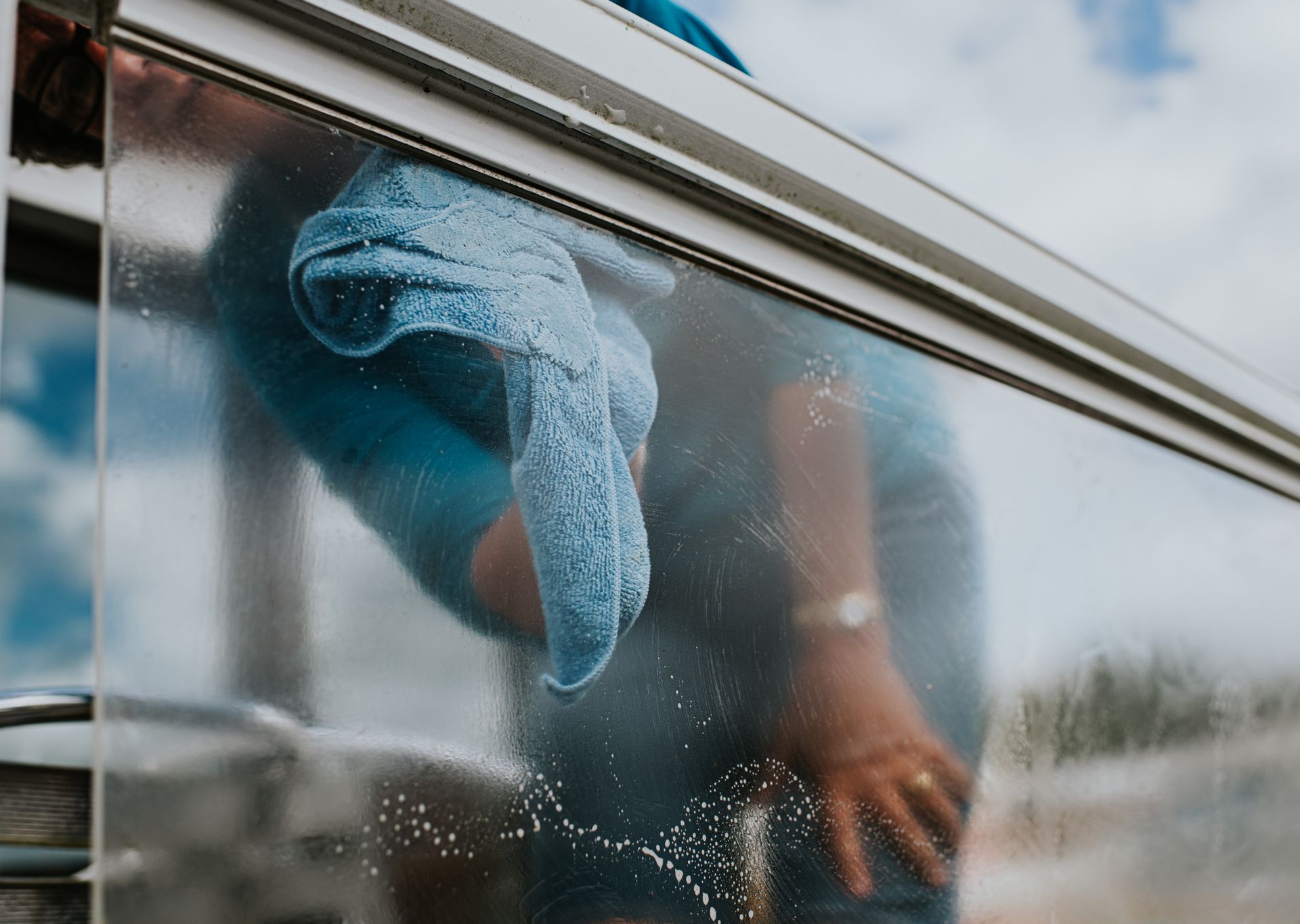 Person wiping down a window with a blue cloth; outdoors.