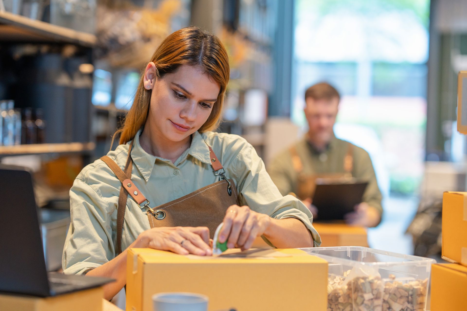 Packing boxes at a store counter with shelves and a laptop in the background.