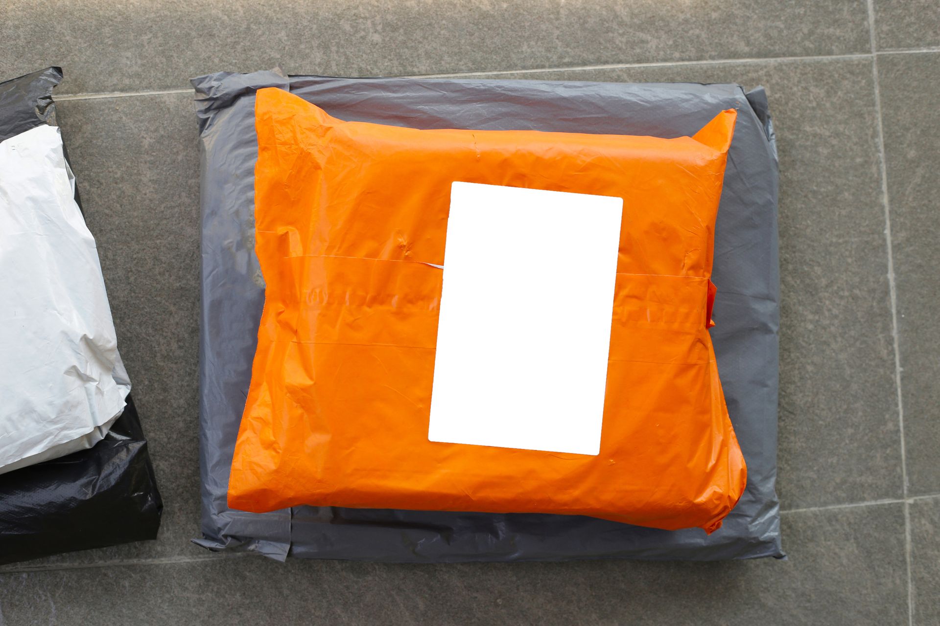 Orange package with a blank white label on a gray package, on a gray tiled surface.