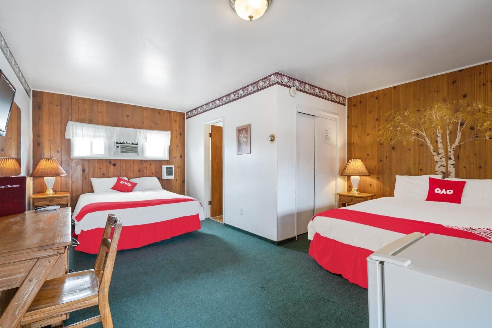 A hotel room with two beds , a desk and a refrigerator