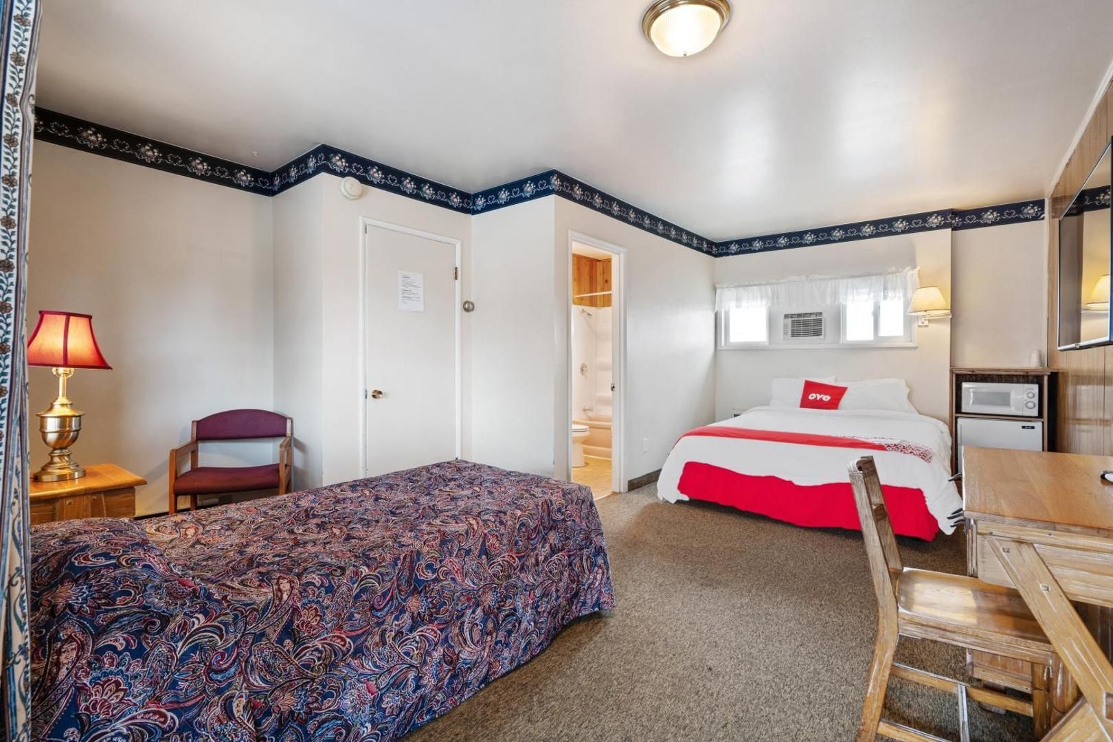 A hotel room with two beds , a desk , a chair and a lamp.