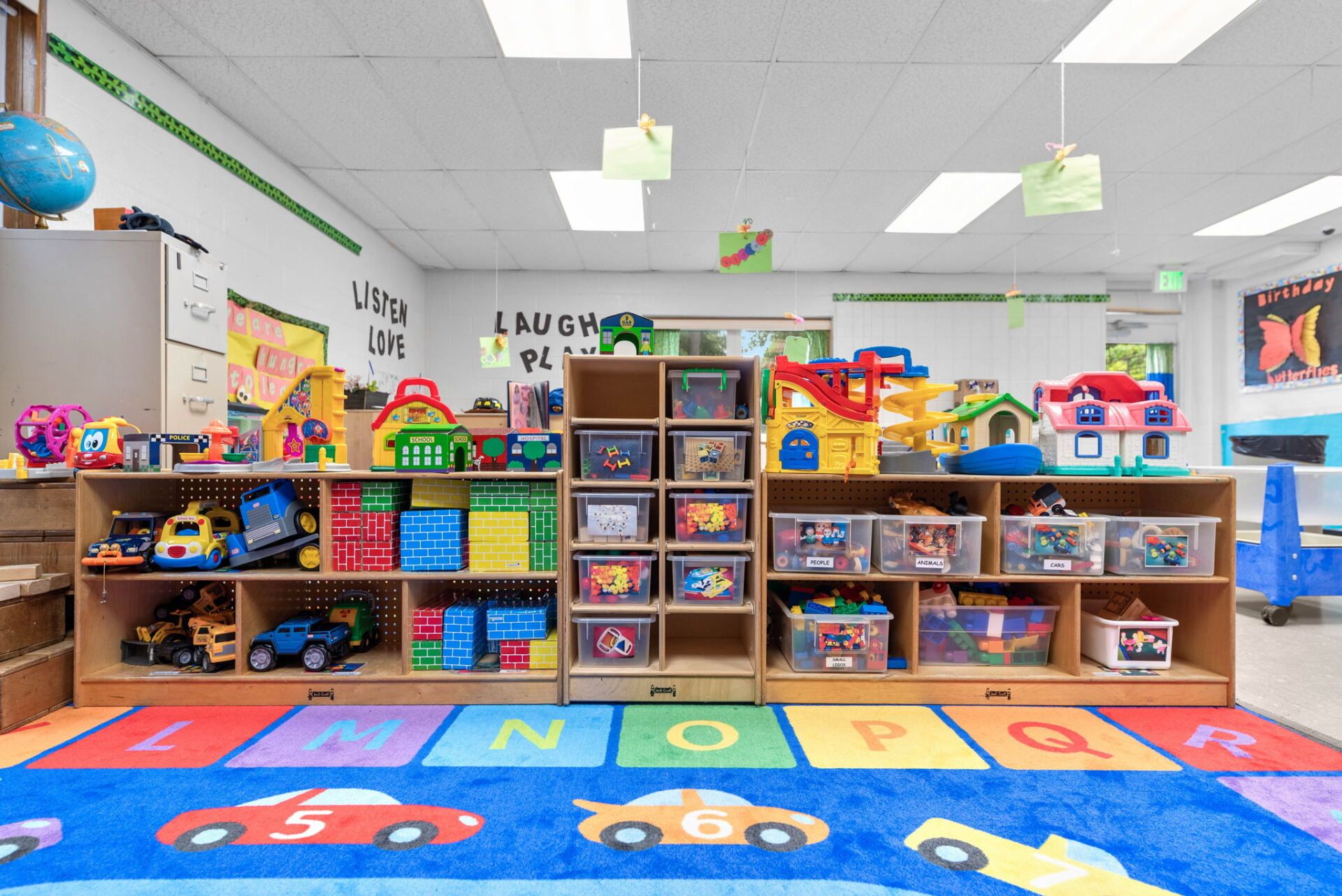 Playroom with shelves of toys, a colorful rug, and decorations.