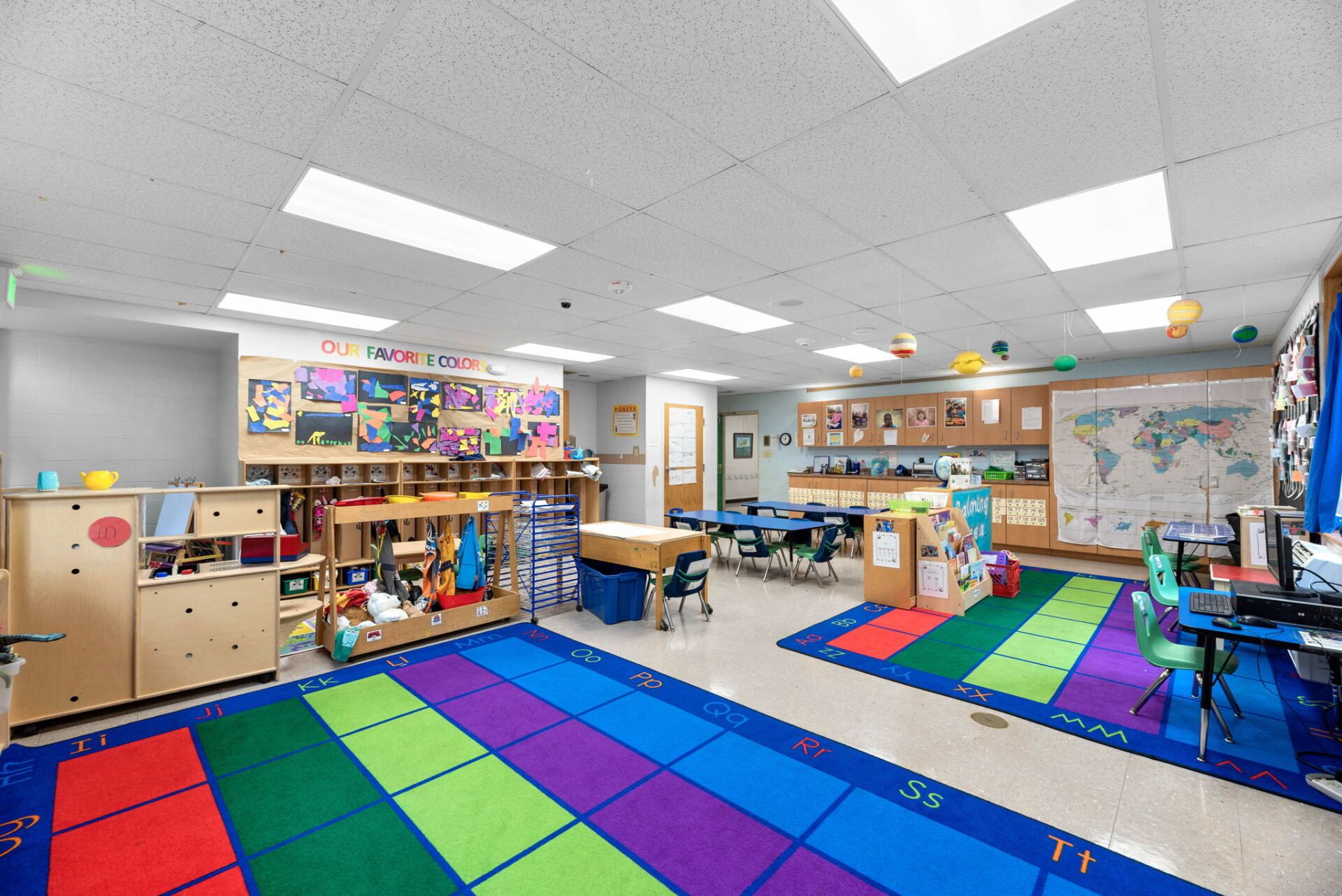 A colorful preschool classroom with rugs, desks, storage, art displays, and a world map.