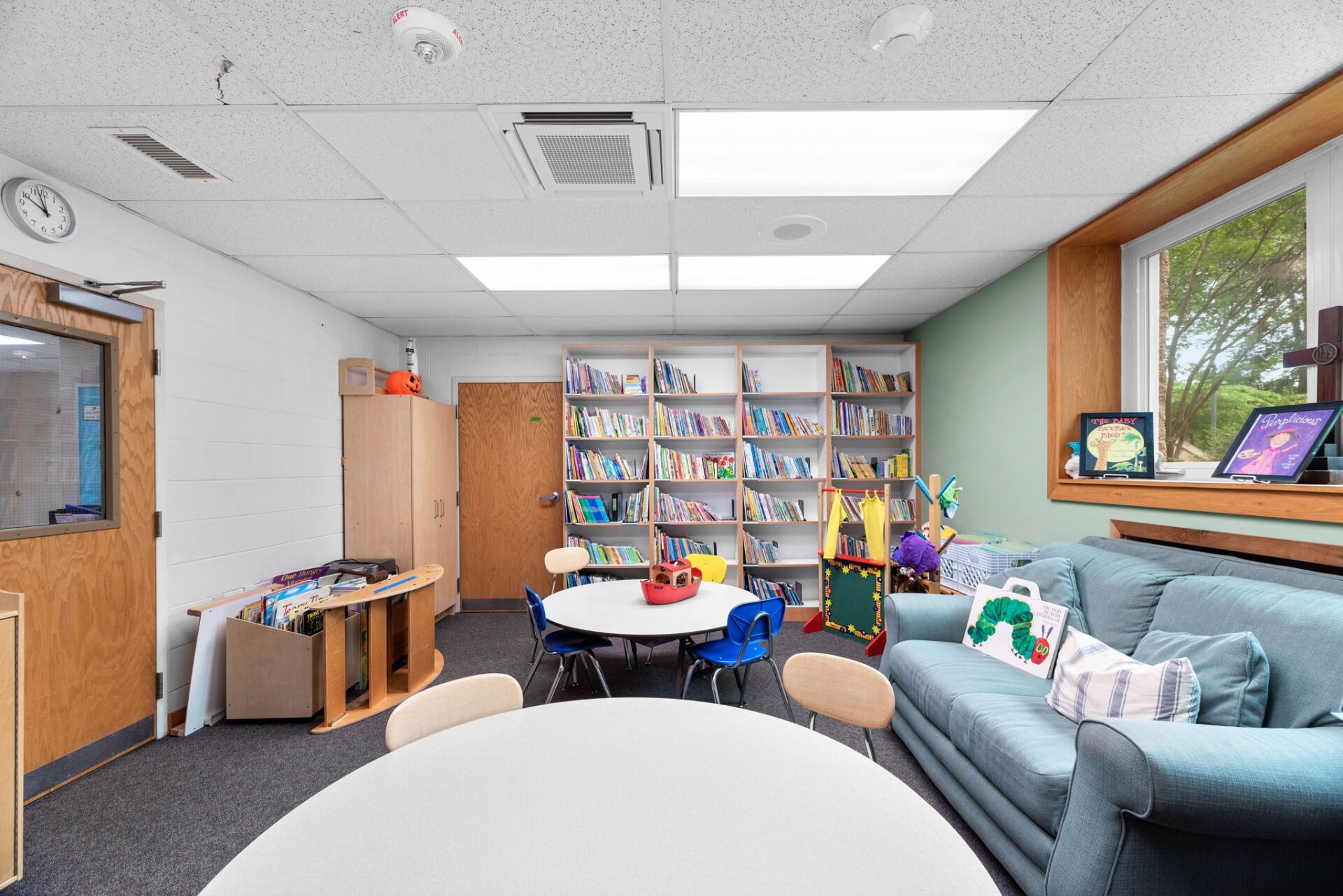A child's library with round tables, a sofa, bookshelves, and a window.