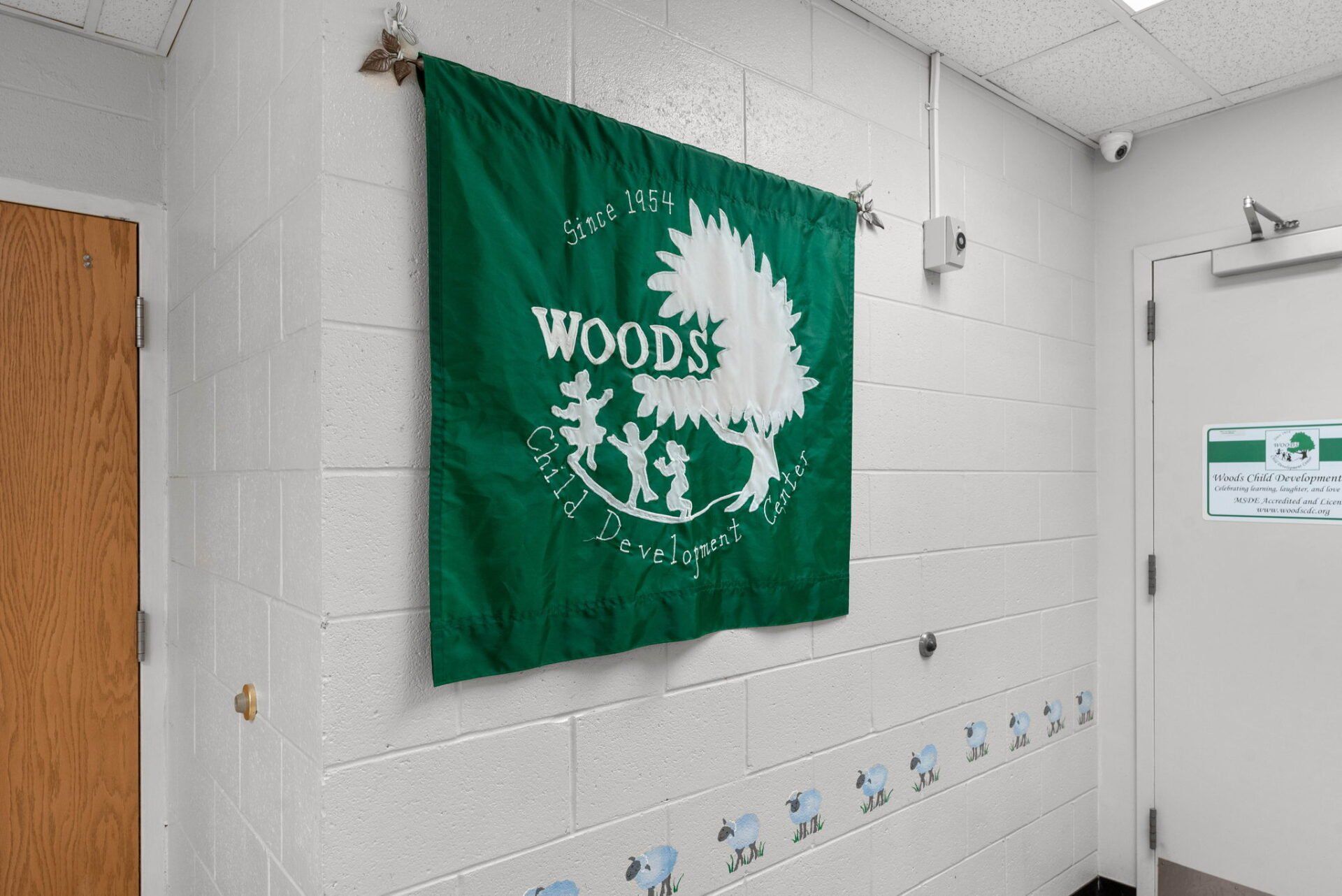 Green Woods Early Learning Center flag hanging on a white brick wall in a hallway.