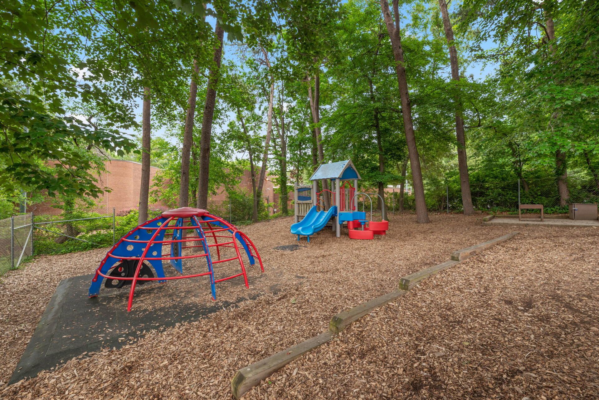 Playground with dome climber, slides, and wood chip ground cover surrounded by trees.