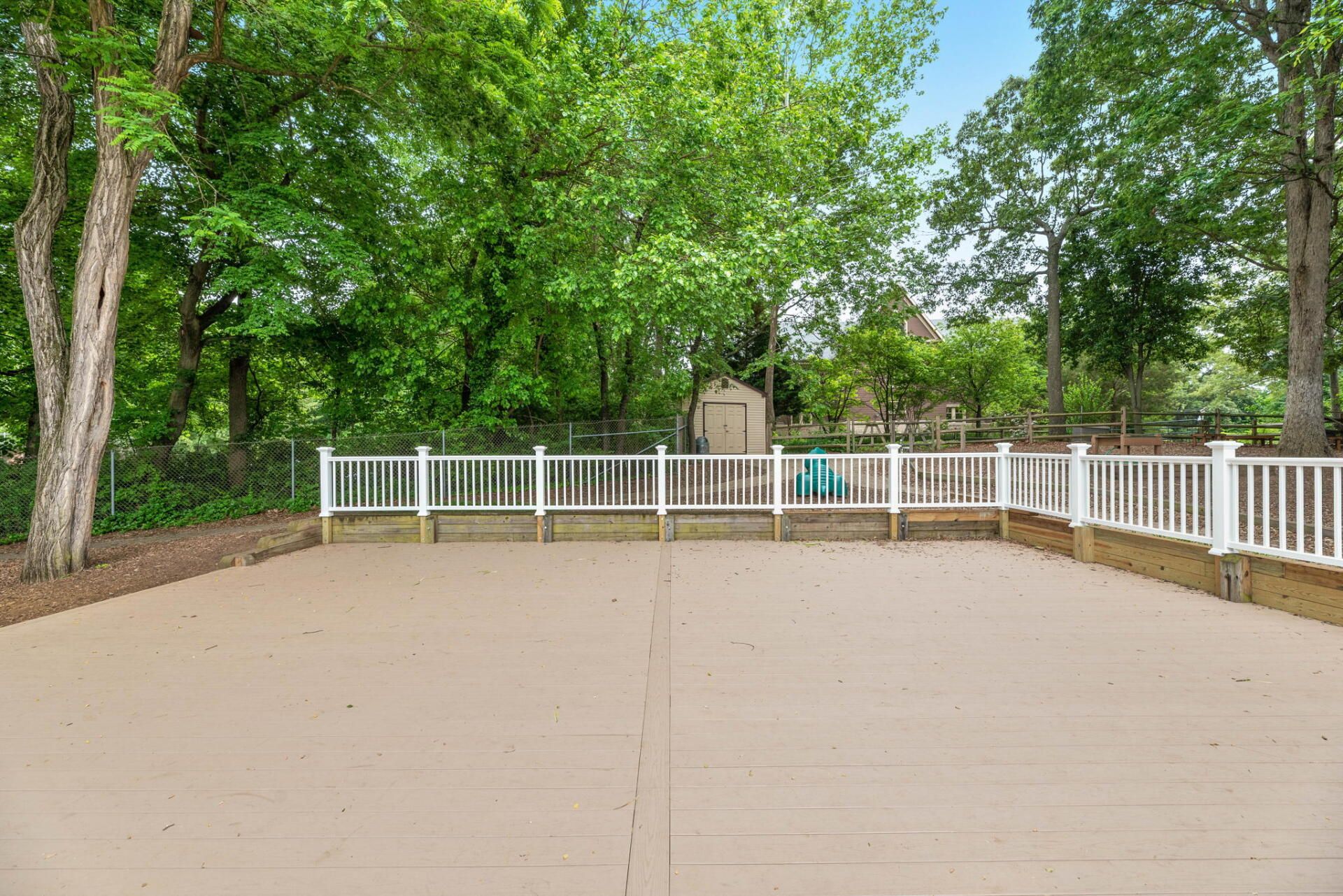 Large, empty wooden deck with white railing, a shed, and trees in the background.