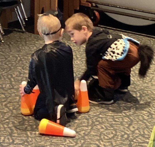 Two young boys in costume play with candy corn; one is in a bat costume and the other is dressed as a horse.