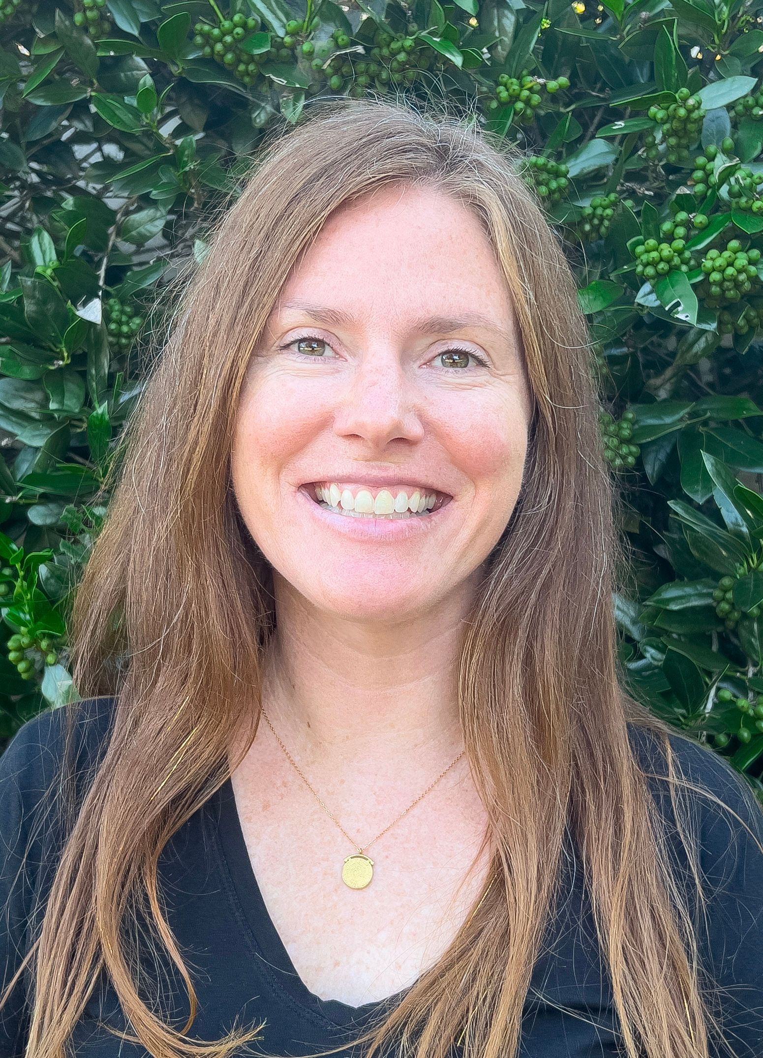 Woman with long red hair smiling, wearing a black shirt, against a dark blue background.