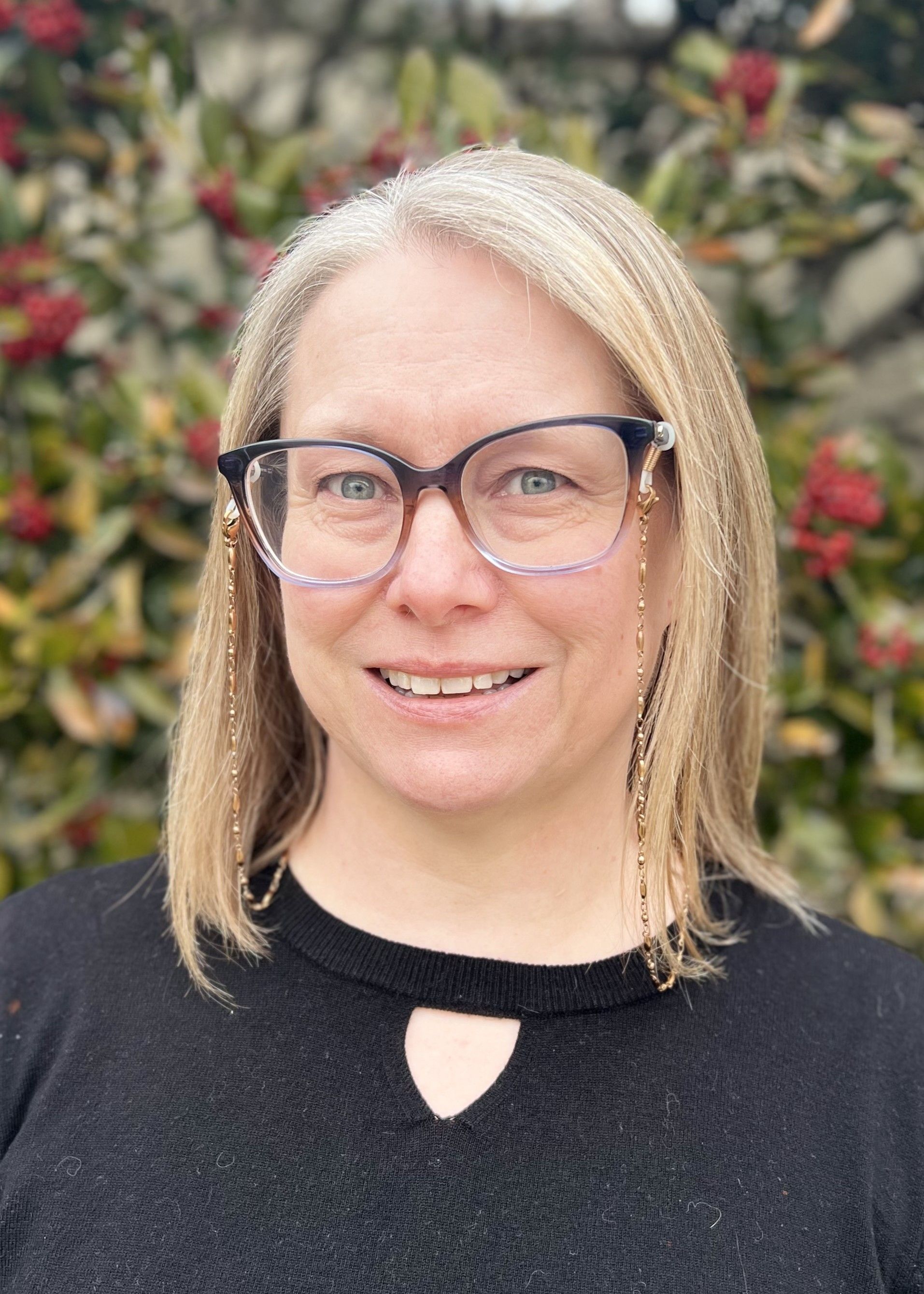 Woman with curly dark hair and a smile wearing a light gray blazer and white top against a blue background.