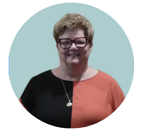 Woman with short curly blond hair wearing glasses and a color-blocked black and orange shirt, smiles at the camera.