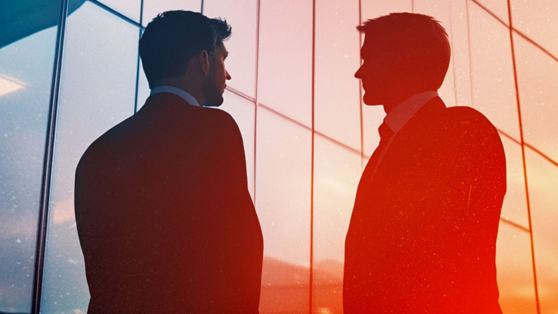 Two people in suits looking at a building's glass windows, possibly discussing something.