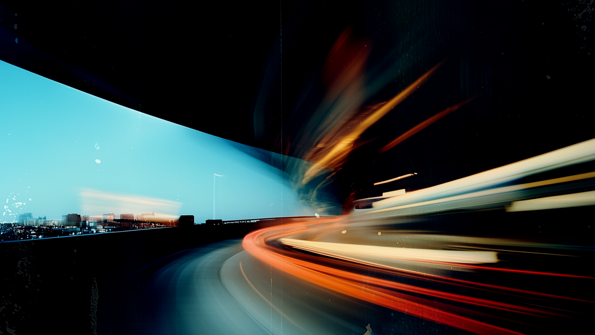 Light trails from vehicles on a curved road at night with city skyline in the distance.