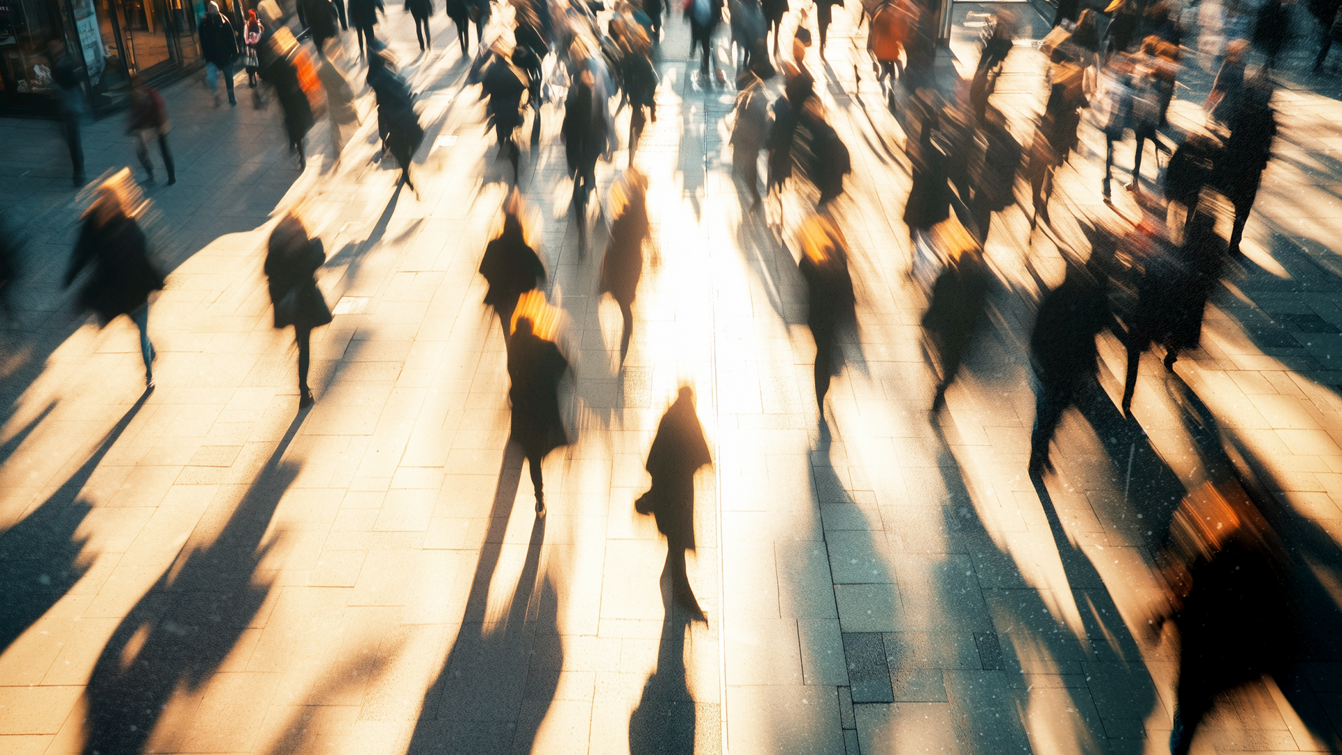 Blurred crowd walking on a sunlit street, long shadows cast by the setting sun.