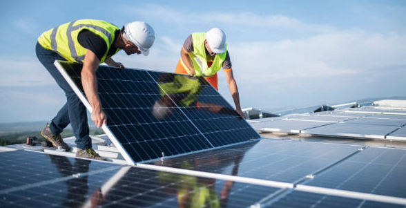 Two workers in vests and hard hats installing a solar panel on a roof.