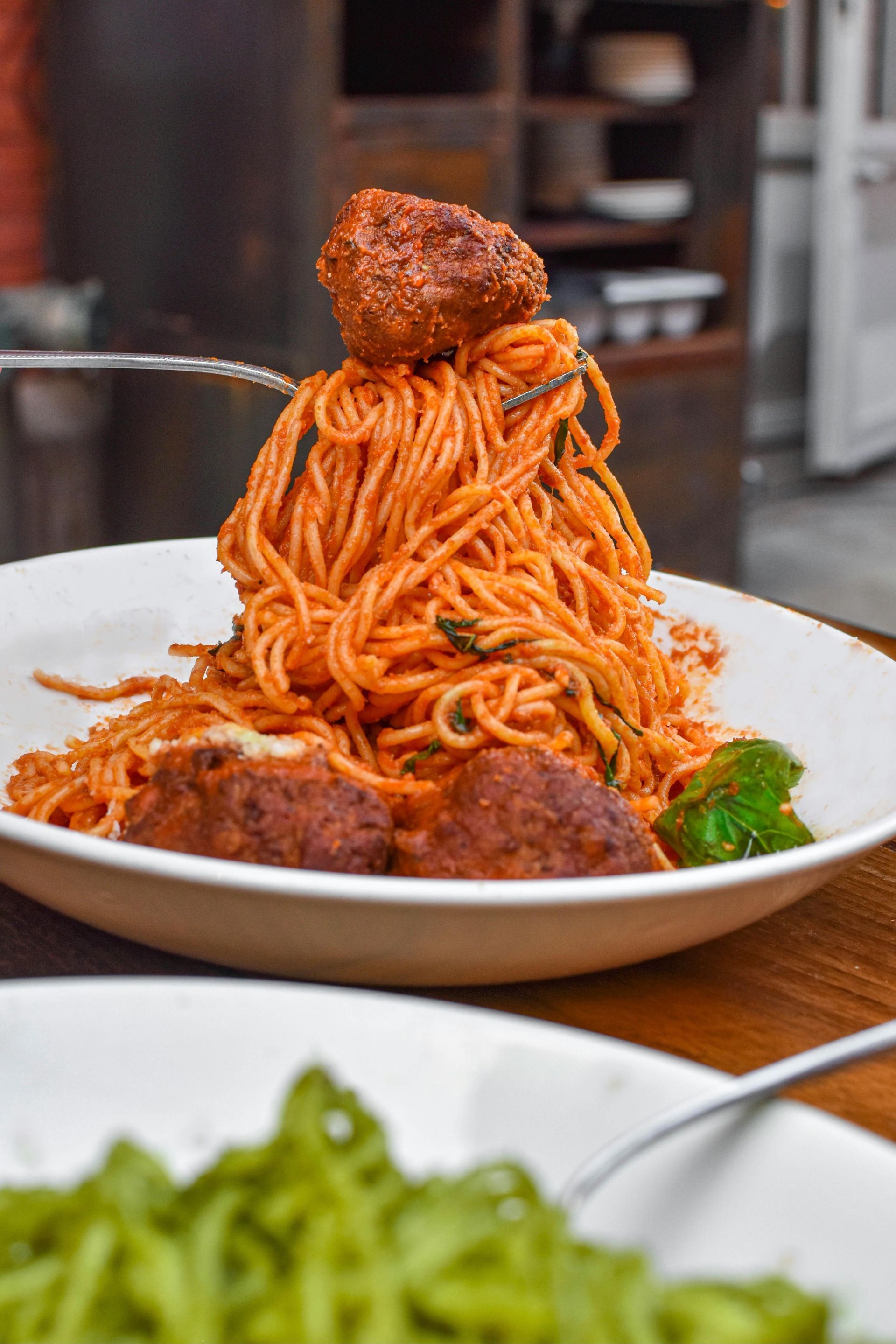A fork lifts a towering mound of red-sauced spaghetti topped with a meatball from a white bowl.