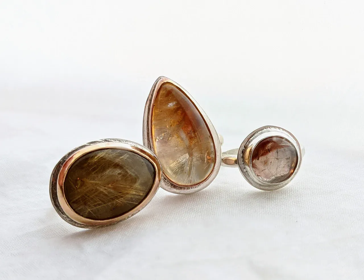 a ring with a brown stone sits next to two other rings