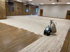 A machine is sanding a wooden floor in a large room.