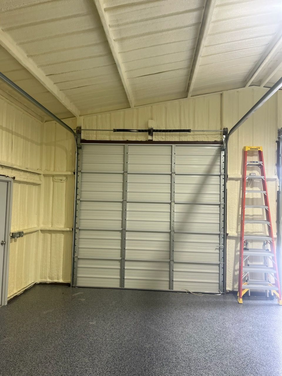 Exterior of a tan building with three closed garage doors. Concrete driveway and sidewalk, bright sunlight.