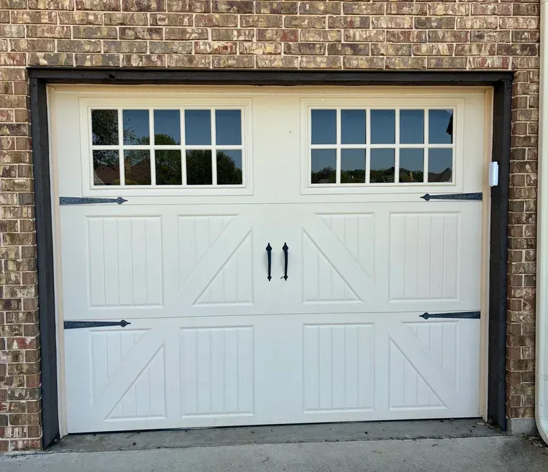 White garage door with windows, black hardware, set in a brick frame.