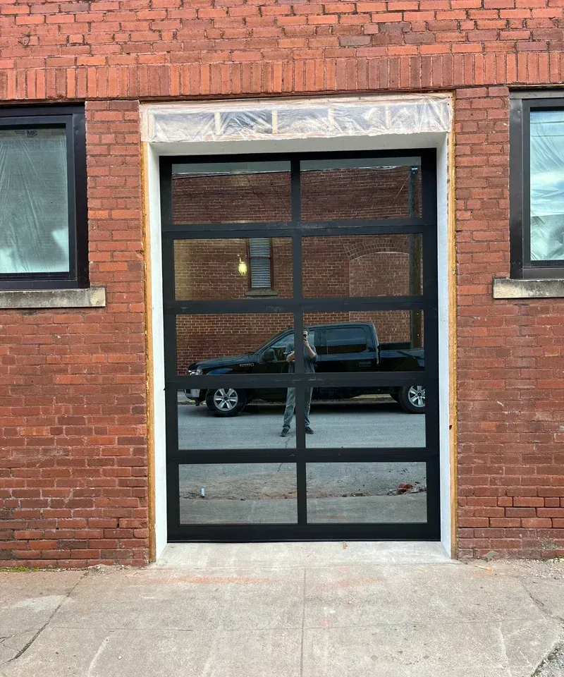 Black framed glass door in a red brick building; a black pickup truck is reflected in the glass.