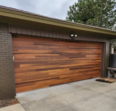 Wooden garage door with horizontal planks, brown brick exterior, and a concrete driveway.