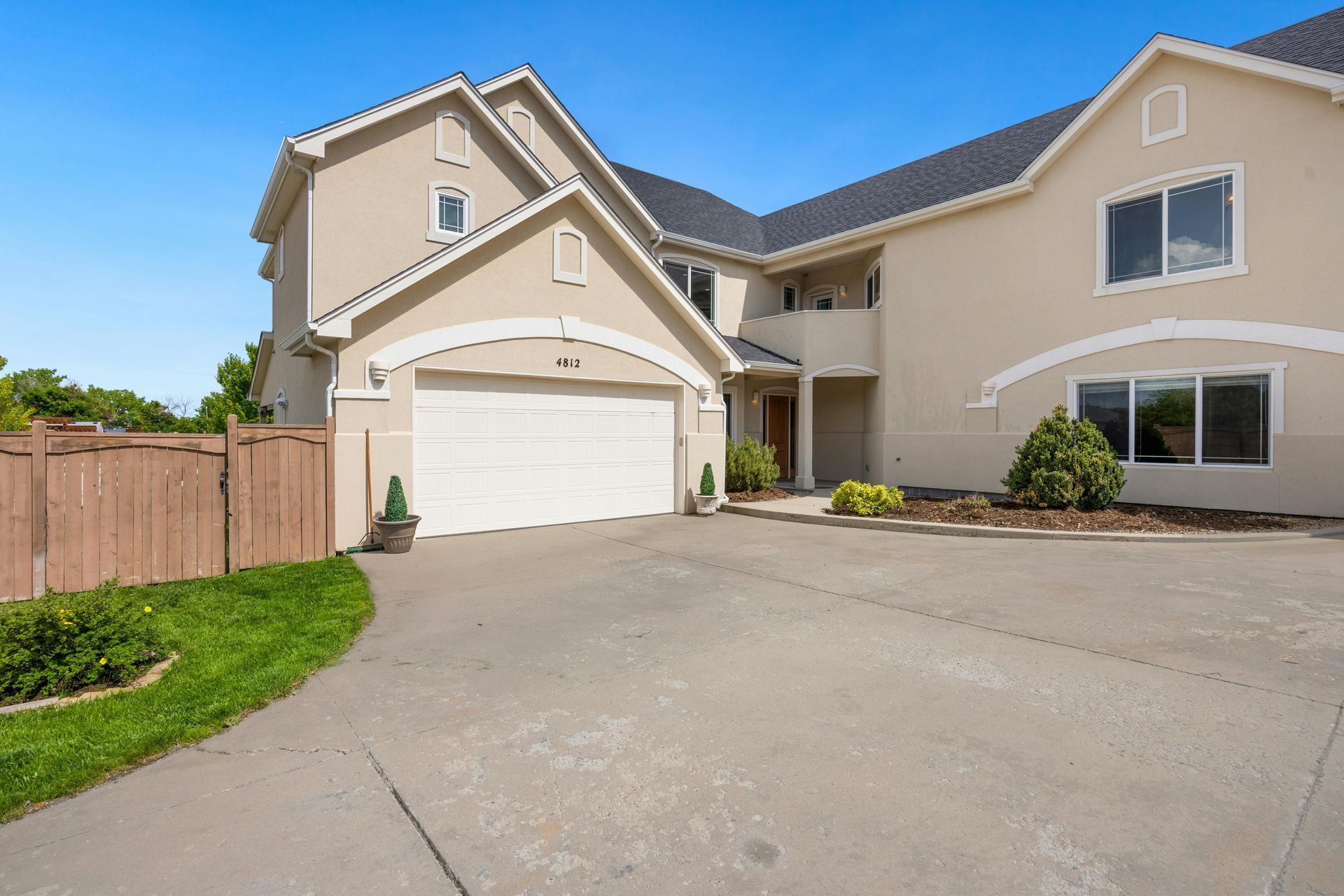 Beige two-story house with a white garage door and concrete driveway on a sunny day.