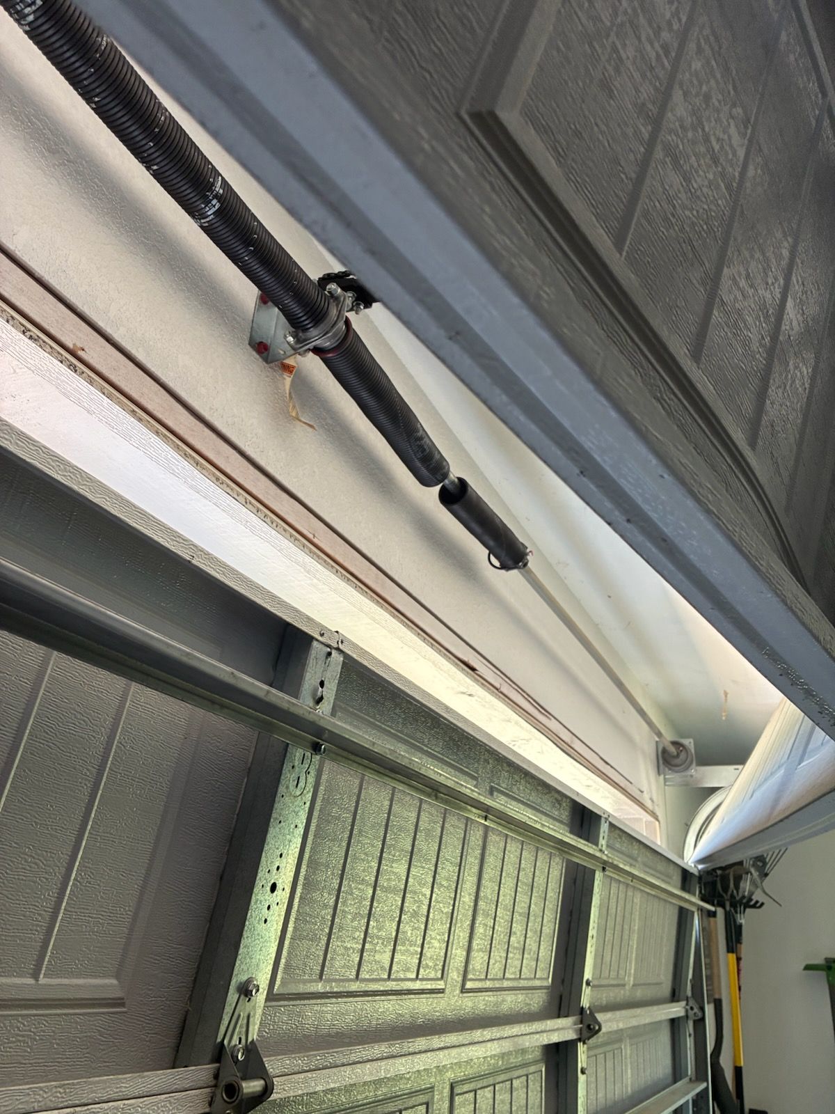 Beige two-story house with a white garage door and concrete driveway on a sunny day.