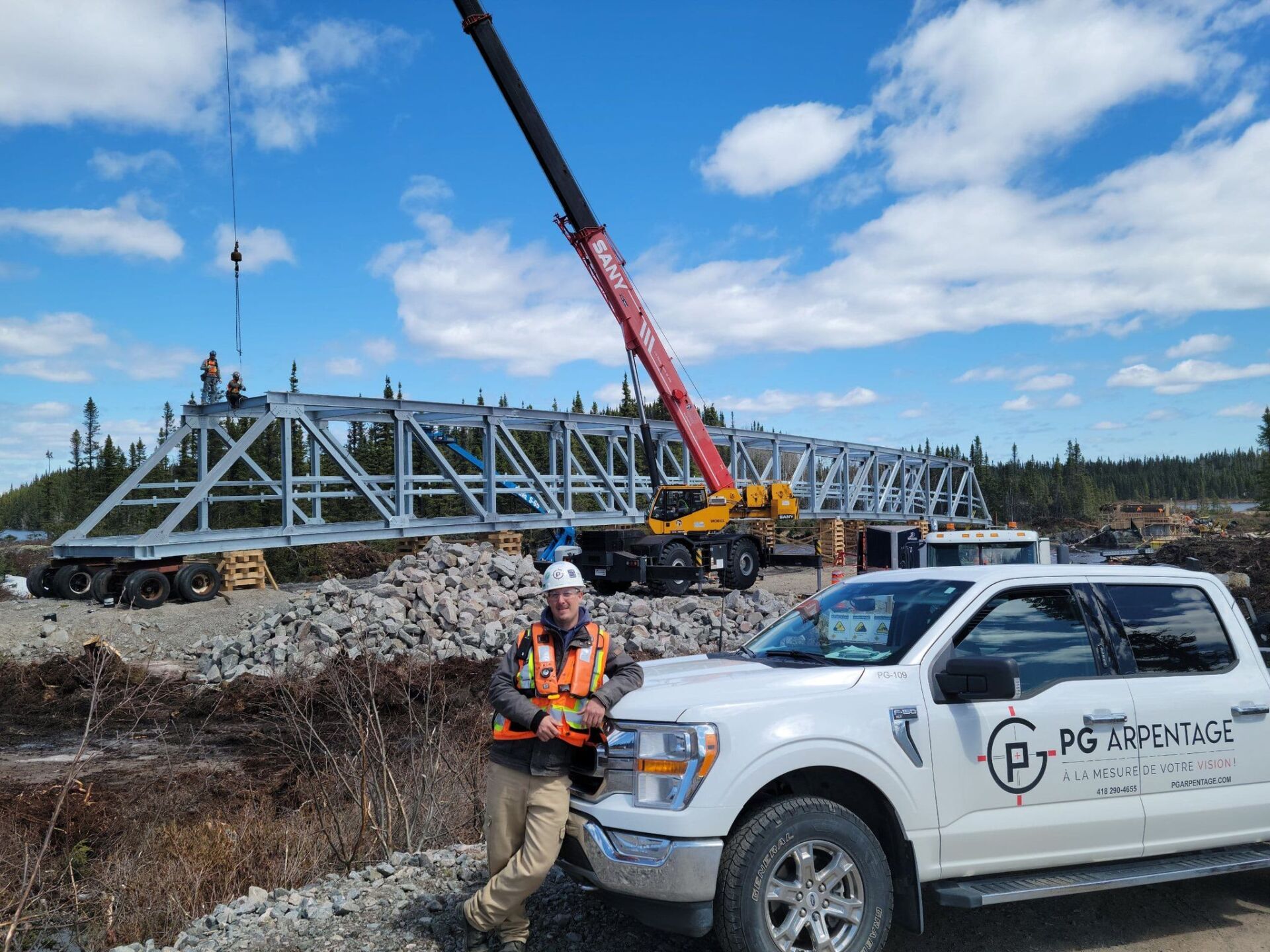 A man is standing next to a truck with a crane in the background.