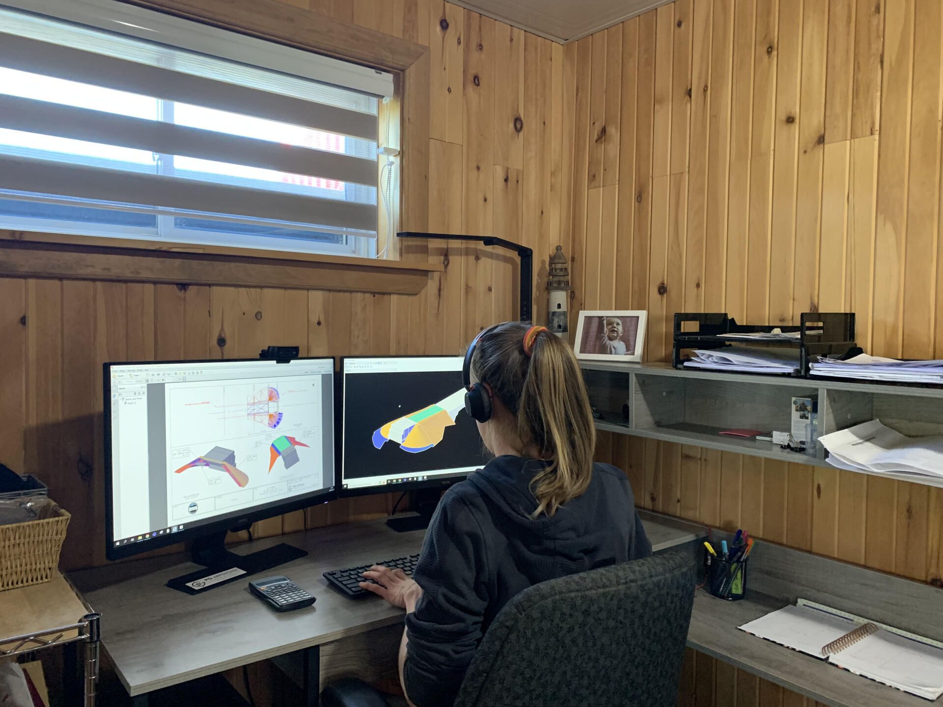 A woman is sitting at a desk in front of two computer monitors.