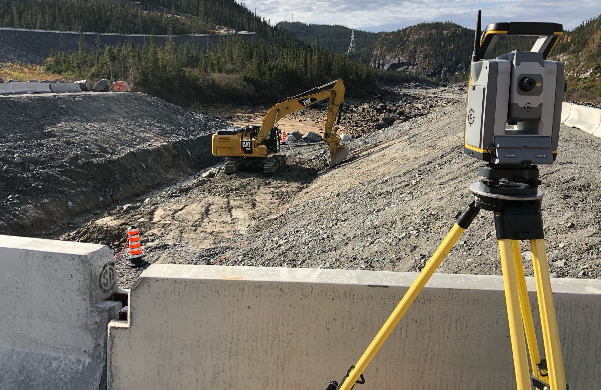 Un appareil d'arpentage sur un trépied surplombant un chantier de construction avec une excavatrice.