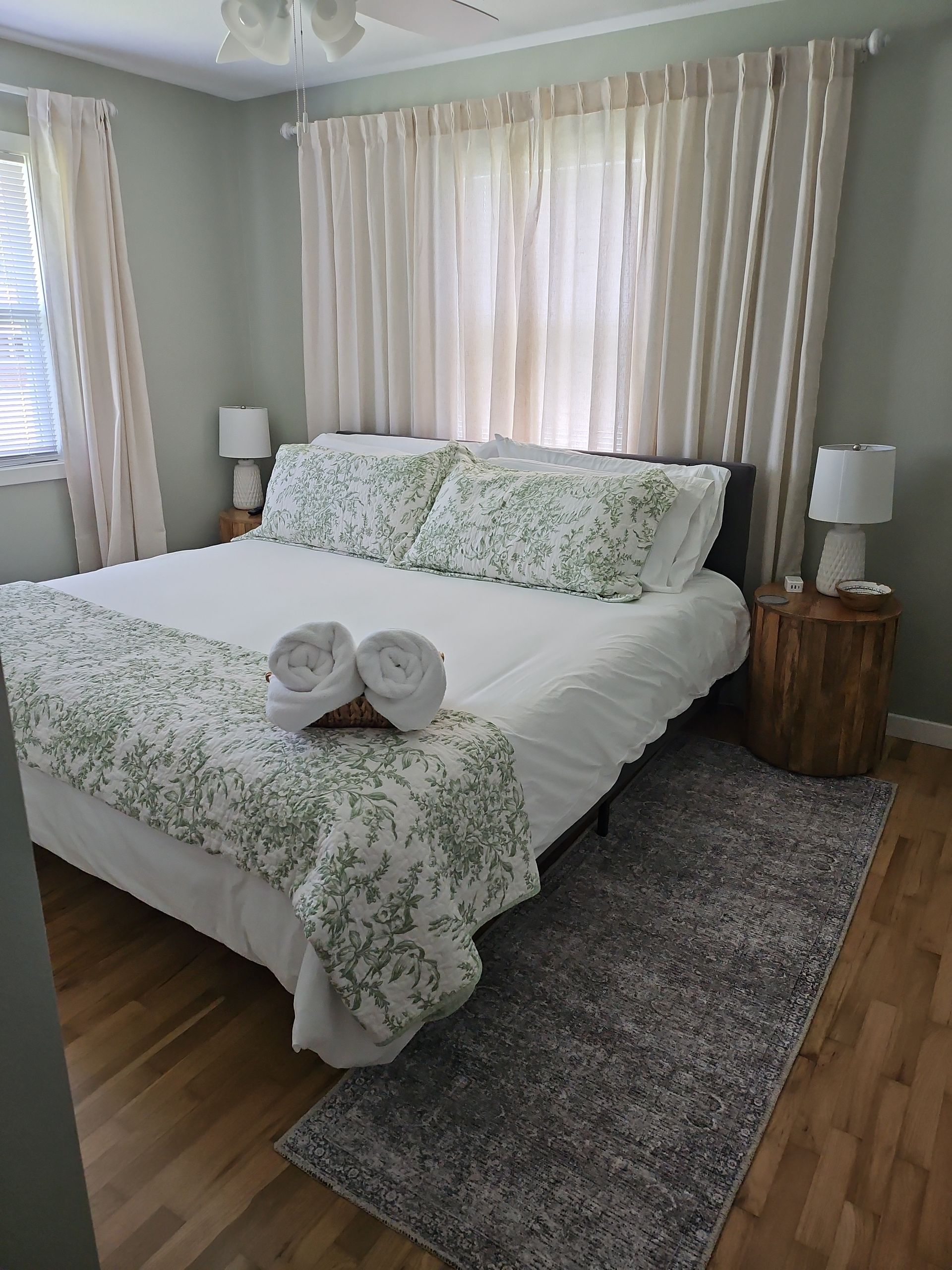 A bedroom with a king size bed , two lamps , a rug and a window.