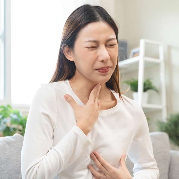 A woman is sitting on a couch with her eyes closed and holding her chest, needing Acid Reflux Treatments.