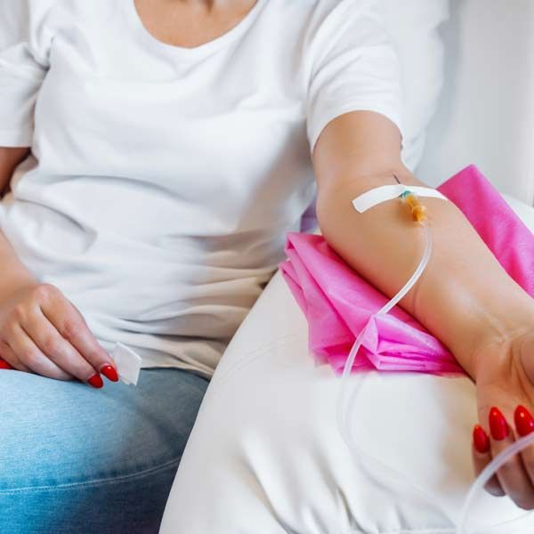 Person receiving Aqua Skin Beauty IV Therapy in the arm, wearing a white shirt and red nail polish.