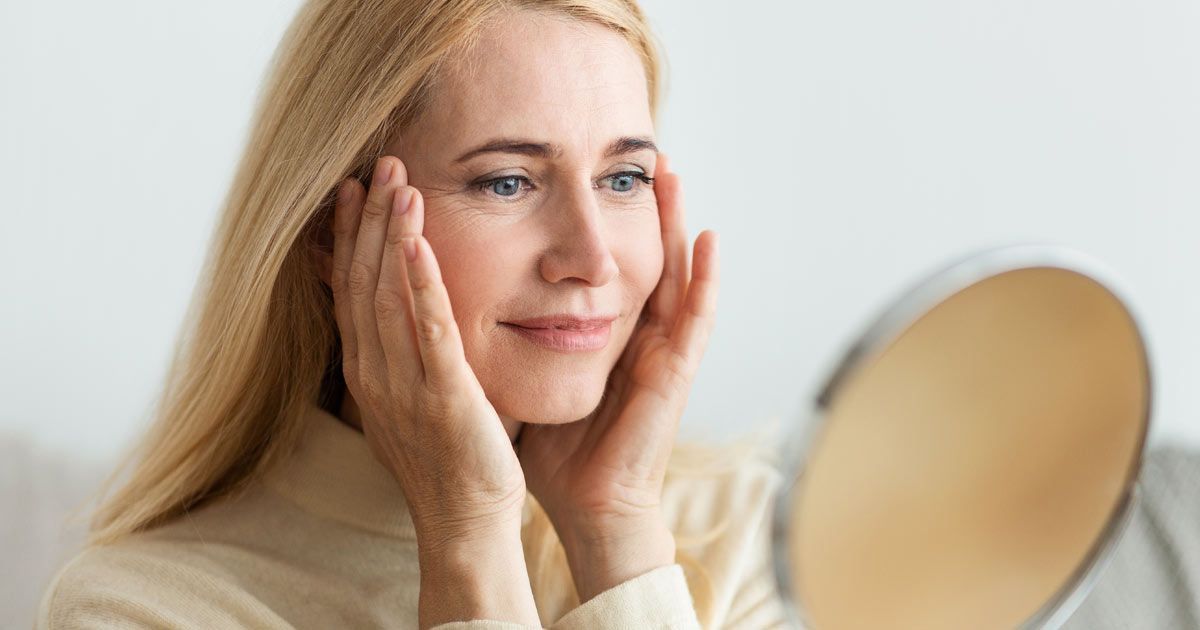 Woman looking in a mirror, touching her face, smiling after her Aqua Skin IV Treatments NYC