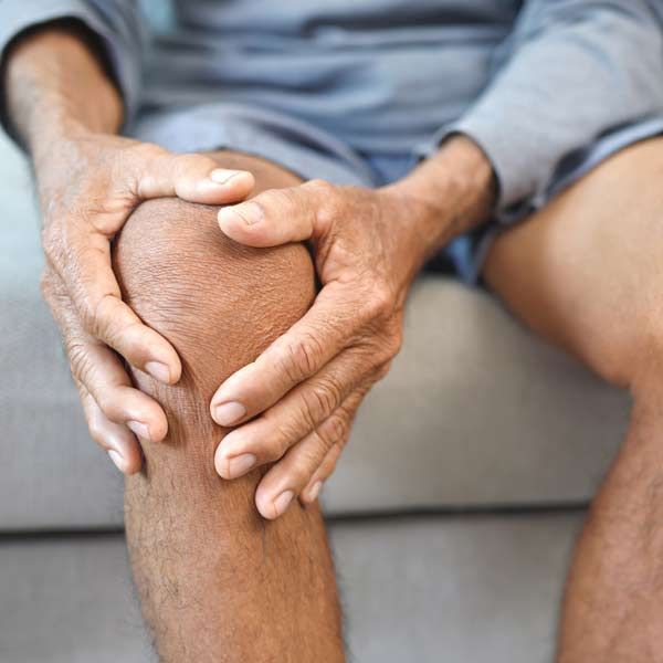 A man is sitting on a couch holding his knee in pain in need of Arthritis Treatments