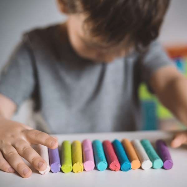 A young boy is playing with a bunch of crayons on a table representing Autism Spectrum Disorder Treatments